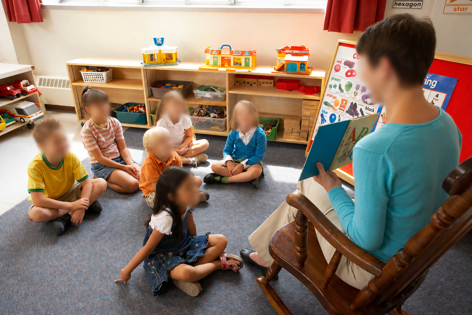 Teacher reading to students seated on a classroom floor; visible faces are blurred.